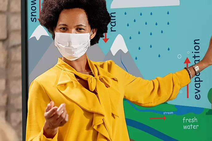 teacher in a face mask standing in front of a procolor board